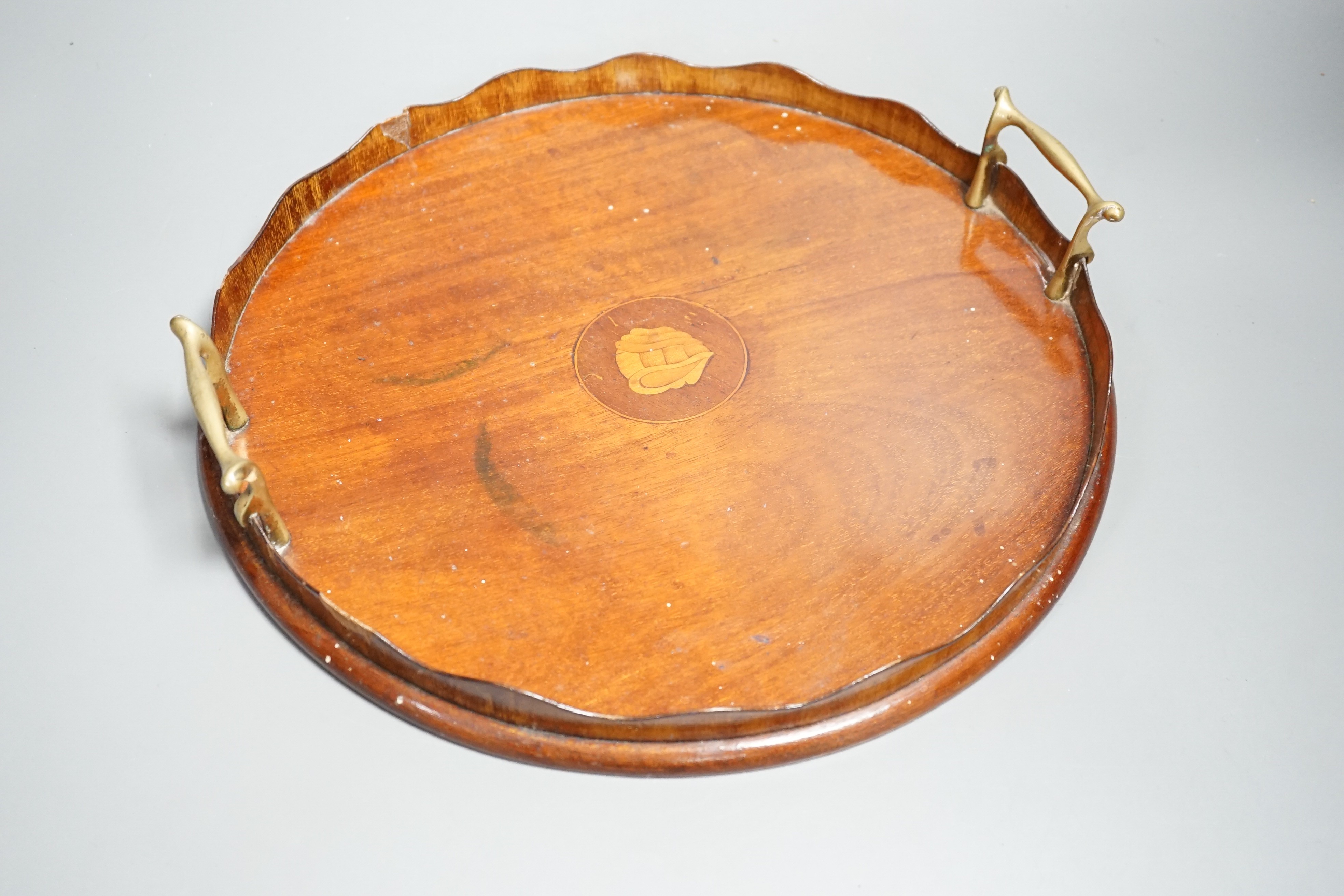 A circular shell inlaid, pie crust edged, brass handled, mahogany tray, 34.5 cms diameter